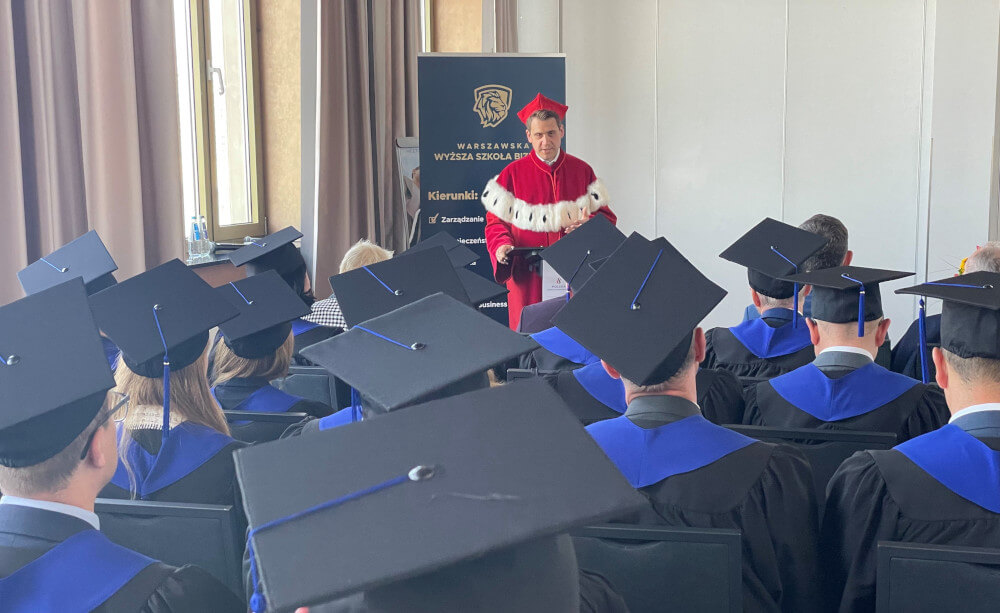 Rektor uniwersytetu, ubrany w czerwoną długą togę z kołnierzem, składa życzenia absolwentom.